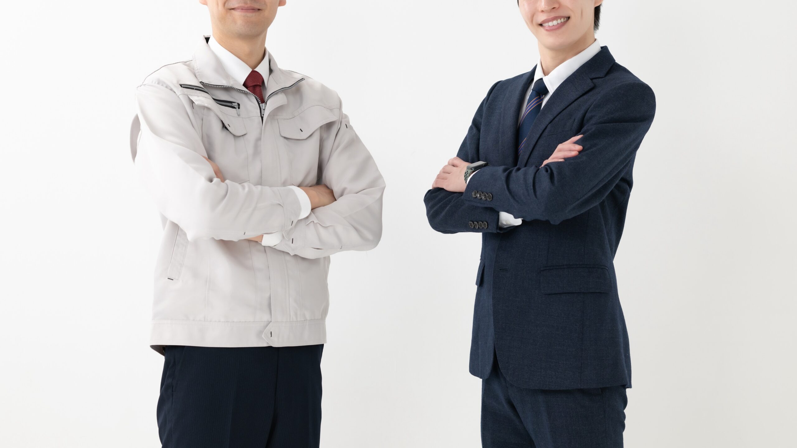 作業着とスーツ姿の2人が腕を組んでいる様子